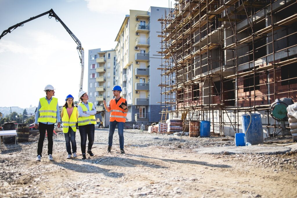 Four people wearing high-visibility vests and hard hats while walking through an active construction site.
