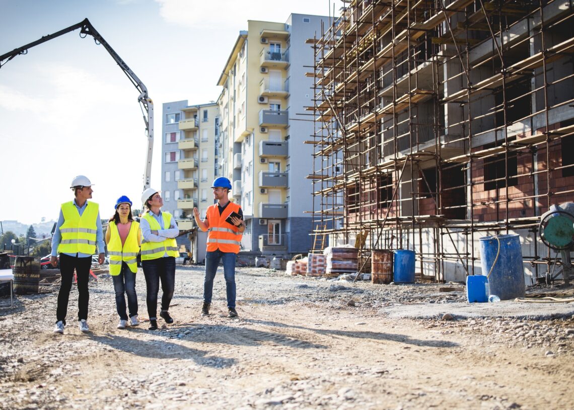 Four people wearing high-visibility vests and hard hats while walking through an active construction site.