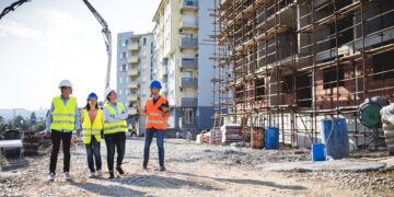 Four people wearing high-visibility vests and hard hats while walking through an active construction site.