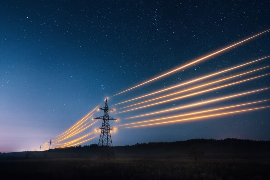 A line of electricity transmission towers at night. The electrical lines between the towers are glowing.