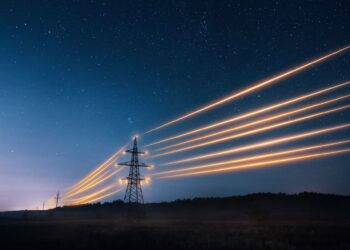 A line of electricity transmission towers at night. The electrical lines between the towers are glowing.
