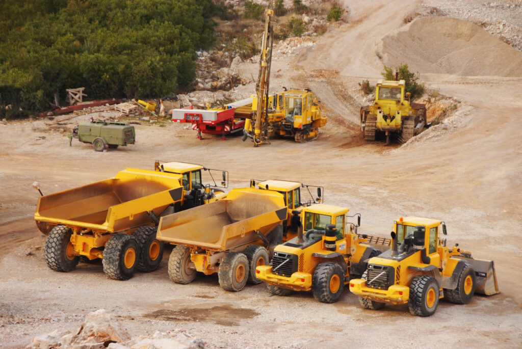 An overhead view of multiple yellow tractors and dump trucks parked in a row at a construction site.