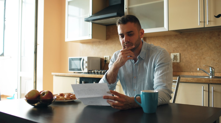 A person reviewing tax paperwork at a kitchen table with a laptop